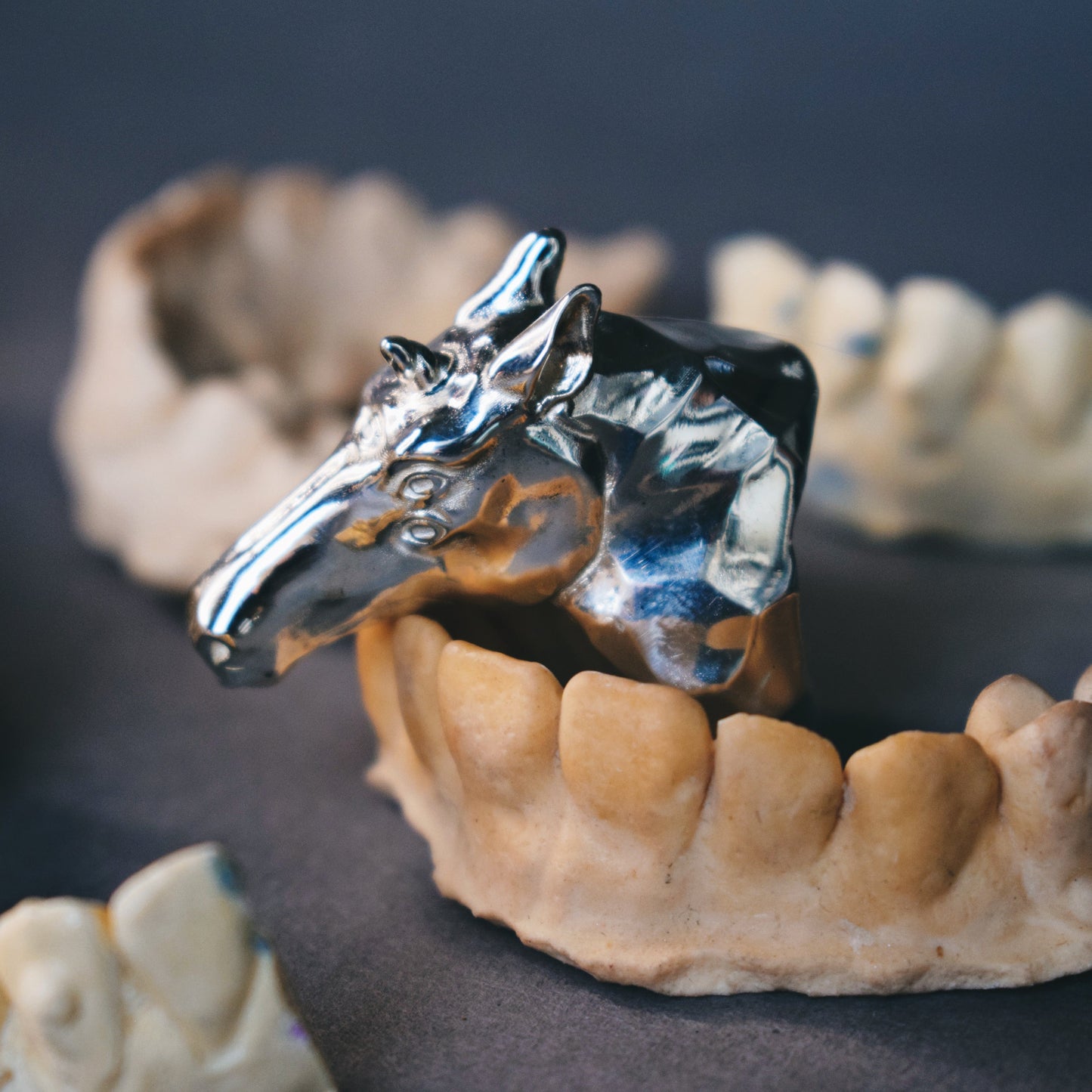 Metallic horse head figure on a set of human dentures against a dark background